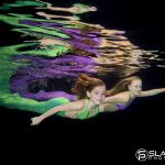 Zwei Mädchen mit Schwimmflossen in grün und lila schwimmen im Becken
