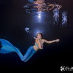 Mädchen mit Schwimmflosse in blau schwimmt im Becken mit Quallen