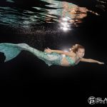 Mädchen mit Schwimmflosse in türkis schwimmt im Becken